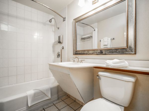 A bright bathroom with a sink, toilet, bathtub, shower fixtures, and a framed mirror with folded towels.