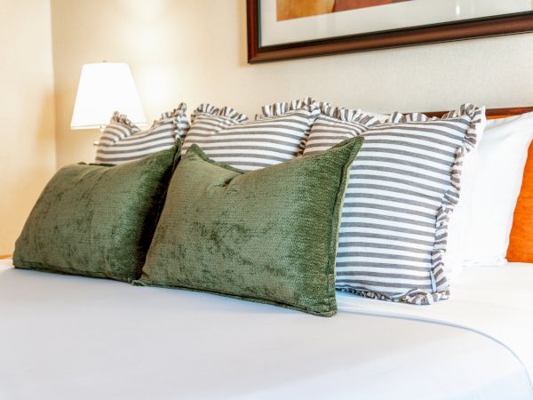 A neatly made bed with green and striped throw pillows, plush bedding, and a lamp in a warm room.
