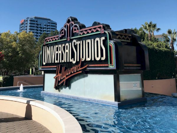 Neon Universal Studios Hollywood sign beside a fountain pool under a clear blue sky.
