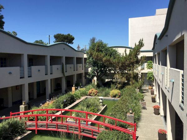 Courtyard with a small pool, landscaped greenery, white buildings, and a red railing under a clear blue sky.