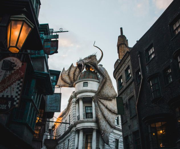 A towering dragon-topped wizard statue outside Gringotts Bank in a magical street, with lanterns and crowds below.