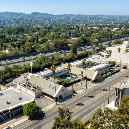 Aerial view of a hillside town with busy highways, parking lots, and commercial buildings in the foreground.