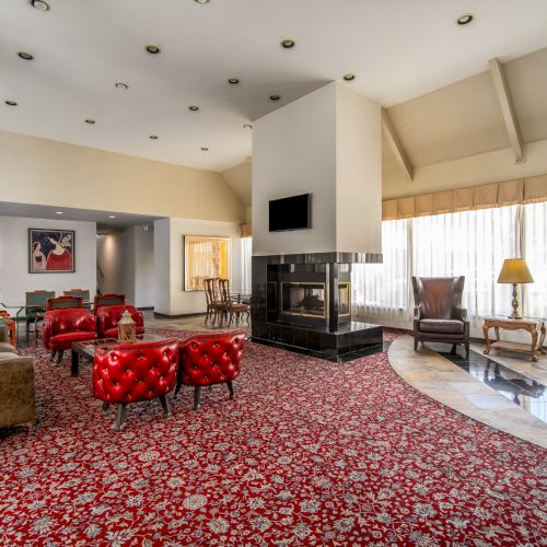 A spacious living room with red patterned carpet, sofas and chairs, a black fireplace, and warm pendant spotlights.