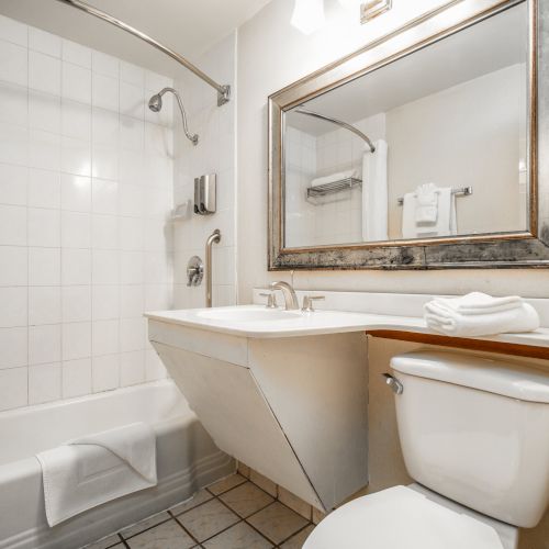 A clean bathroom with a bathtub, sink, chrome faucets, white towels, and a large mirror above the toilet.