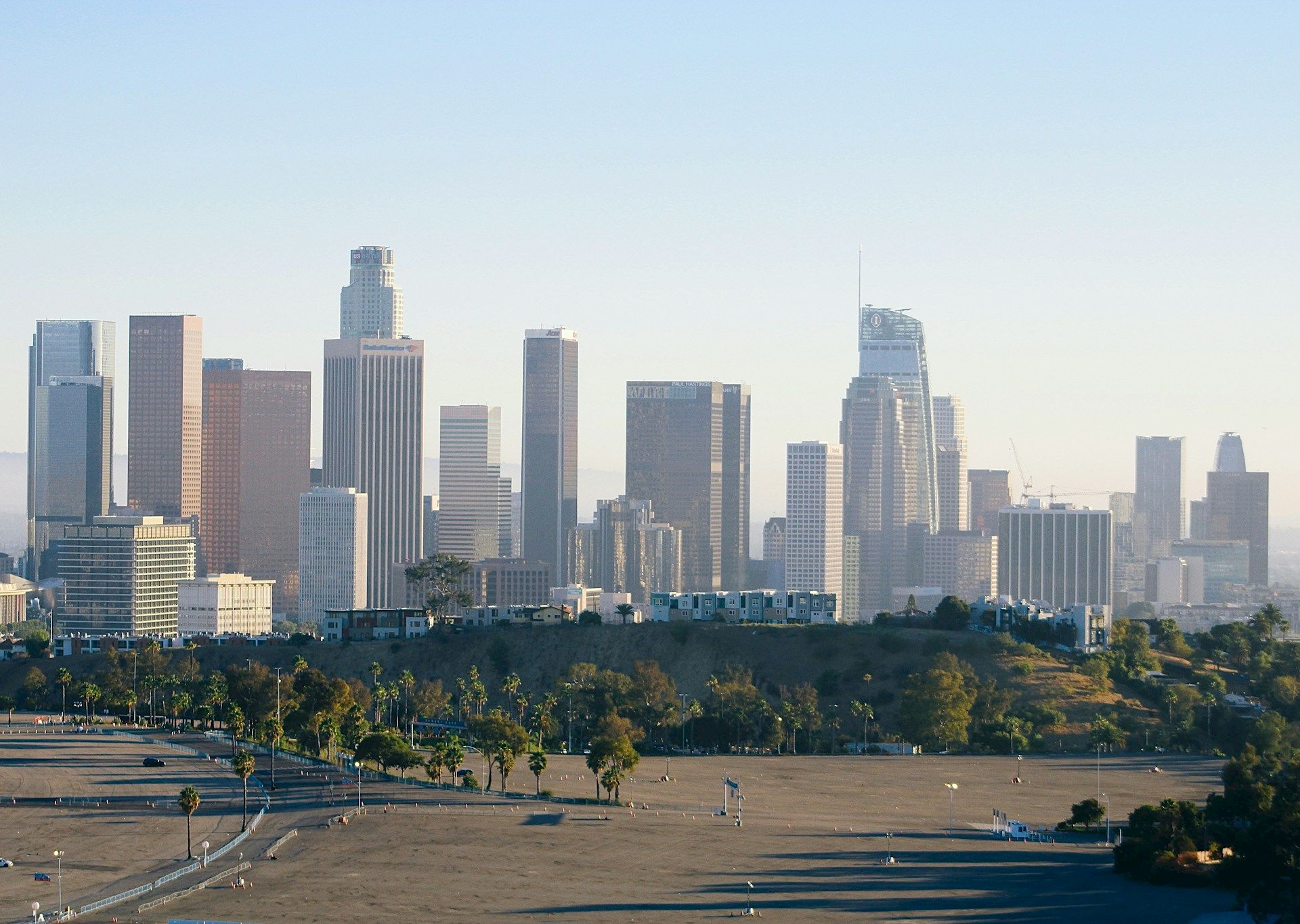 Downtown Los Angeles skyline with high-rise office towers, clear sky, and a grassy park in the foreground.