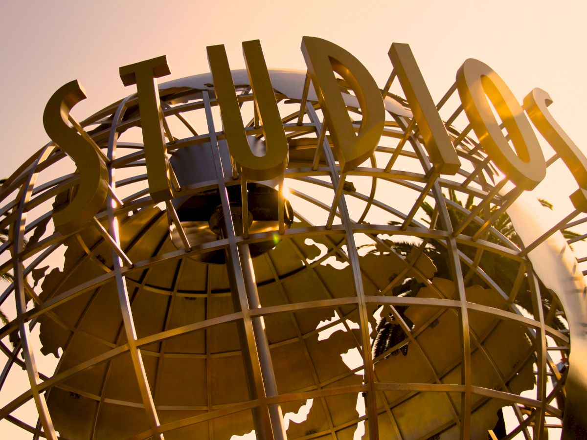 Giant raised metal letters atop an amusement-park roller-coaster structure, framed by a bright sky.